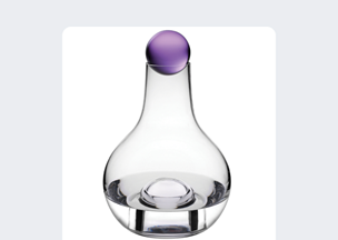 Beyaz arka plan önünde, camdan yapılmış şeffaf bir sürahi duruyor, alt kısmı geniş, boynu dar, üst kısmında mor renkte mat bir küre kapağı bulunuyor.