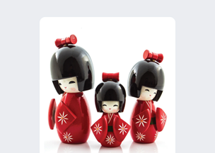 Beyaz arka plan önünde, üç adet geleneksel Japon tarzı tahta bebek yer alıyor, hepsi kırmızı kimono giymiş, siyah parlak saçlara sahip, üzerlerinde beyaz çiçek desenleri, ortadaki figür daha küçük boyda. 