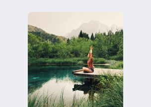 Doğal manzarada, ahşap bir iskele üzerinde oturmuş bir kadıni kollarını yukarı kaldırmış, çevresinde yeşil bitkiler ve berrak su bulunuyor. Arka planda dağlar uzanıyor.