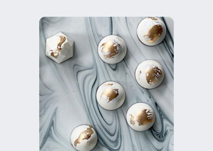 Mermer desenli yüzey üzerinde, beyaz zeminde altın yaldızlı desenlerle süslenmiş altı yuvarlak obje ve bir köşede çokgen biçimli bir parça yer alıyor.