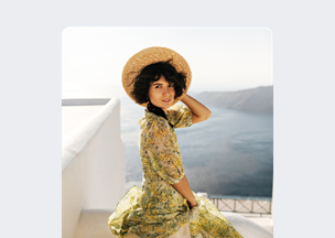 Açık renkli zemin üzerinde, deniz manzarasına karşı oturan 30’larında bir kadın, başında hasır şapka, üzerinde sarı ve yeşil çiçek desenli bir elbise bulunuyor, yüzü gülümser biçimde kameraya dönük.